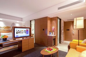 A modern hotel room with a flat-screen TV, wooden furniture, a dining table with fruit, and a sofa. - Hampton BY Hilton Yangzhou Slender (Yangzhou)