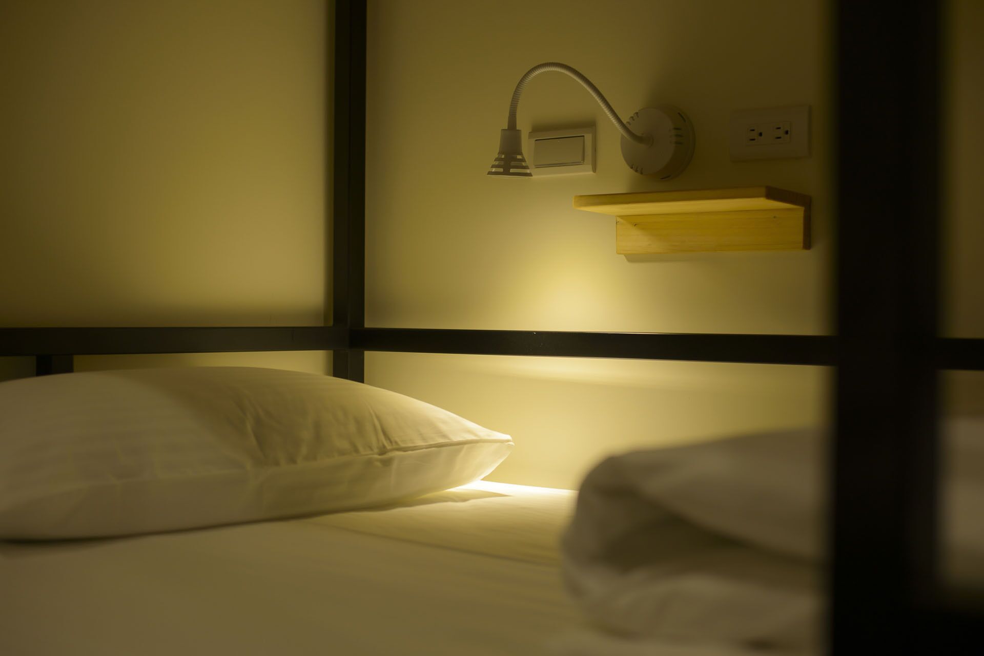 A single bed with a white pillow and a headboard with a built-in shelf.