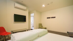 Habitación de hotel con cama, escritorio, silla, televisor y aire acondicionado.