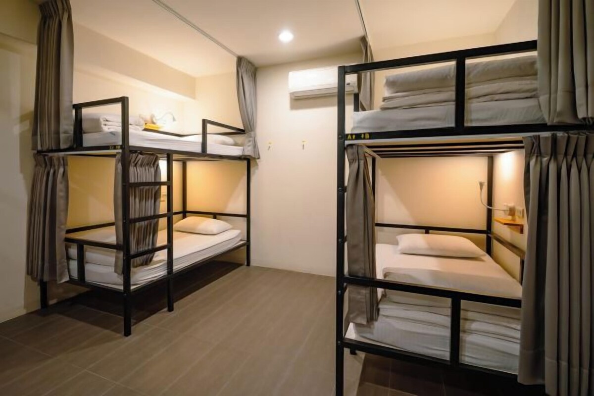 A dormitory room with bunk beds, a small table, and a shelf.