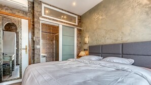 Un dormitorio con una cama grande, una mesita de noche con lámpara, un armario y un baño con paredes de ducha estampadas.
