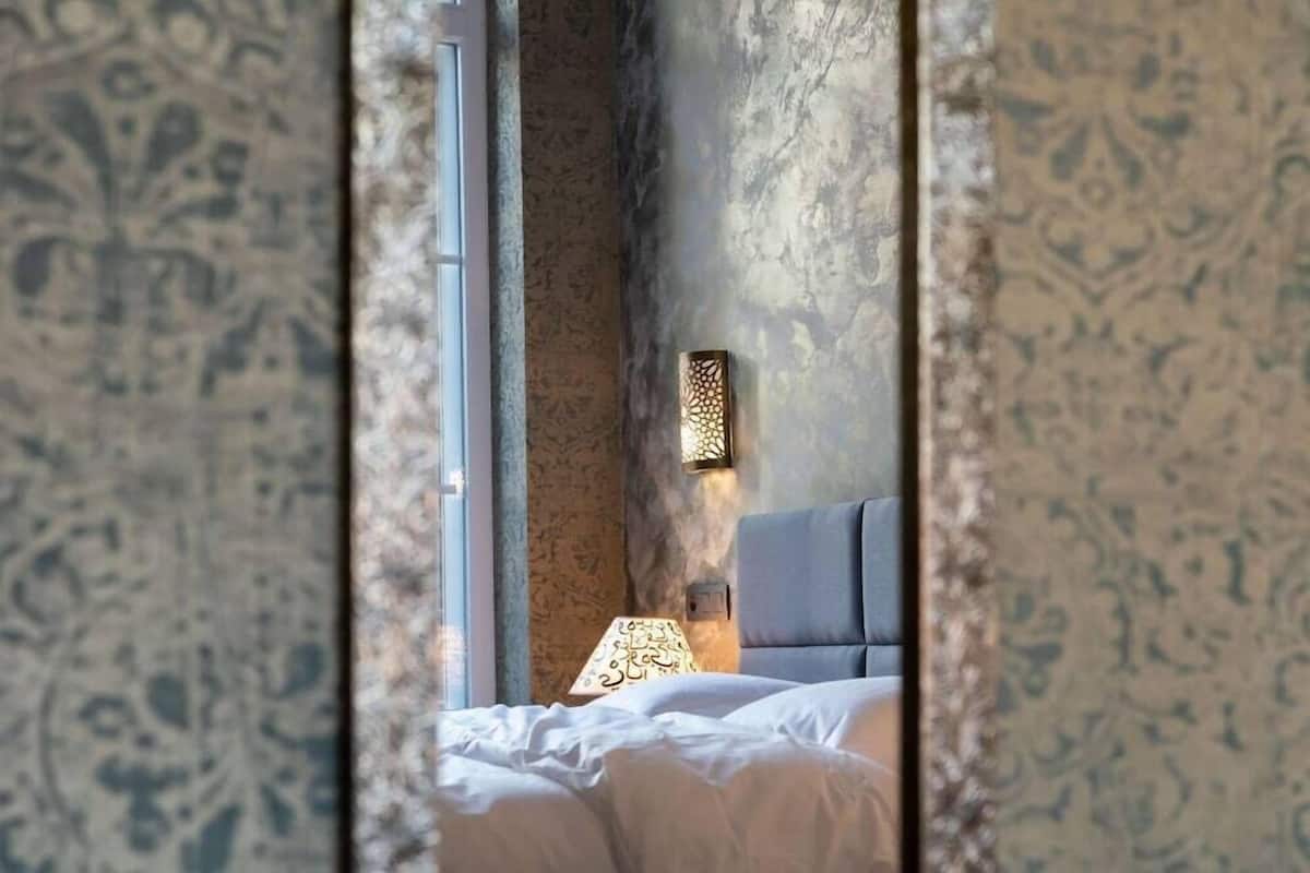 A bedroom with a bed, a nightstand, a wall-mounted lamp, and a window.