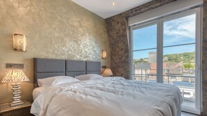 Un dormitorio moderno con una cama grande, dos lámparas de noche y vistas de la ciudad a través de un ventanal.
