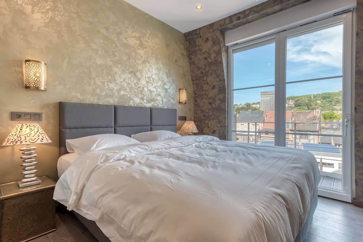 A modern bedroom with a large bed, two bedside lamps, and a view of the city through a large window.