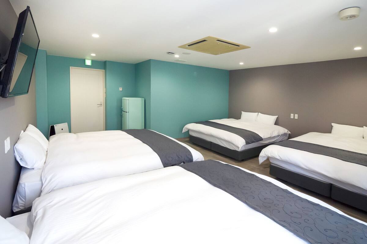 A hotel room with three beds, a flat-screen TV mounted on the wall, and a small refrigerator.
