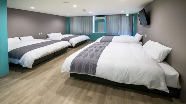 A hotel room with three beds, a TV mounted on the wall, and a window with curtains. - 88HOTELS (Matsuyama)