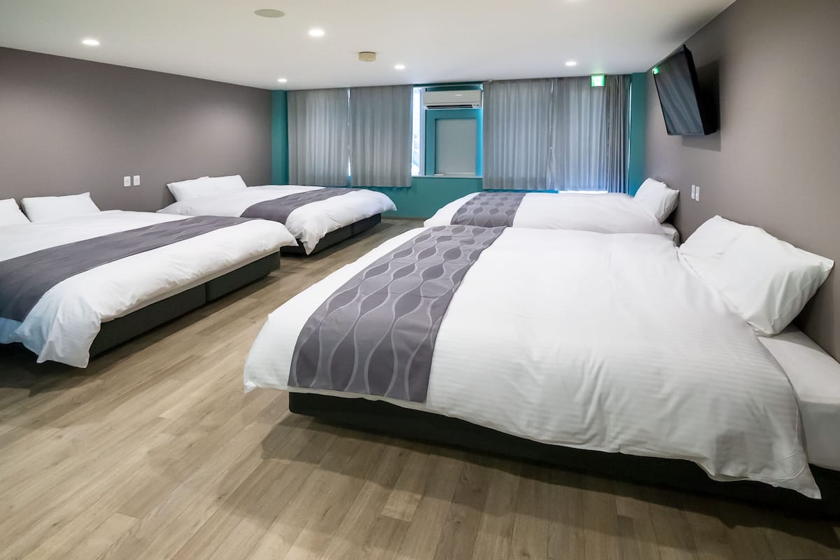 A hotel room with three beds, a TV mounted on the wall, and a window with curtains.