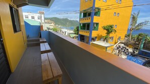 A balcony with wooden benches, overlooking a street with buildings and a view of the sea. - B'Fin Hostel Lanyu (Lanyu)