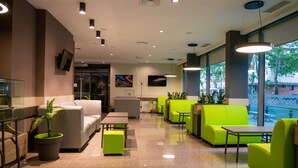 A modern lobby with seating areas, a reception desk, and large windows offering a view of the street. - Hotel Puldin COOP (Plovdiv)