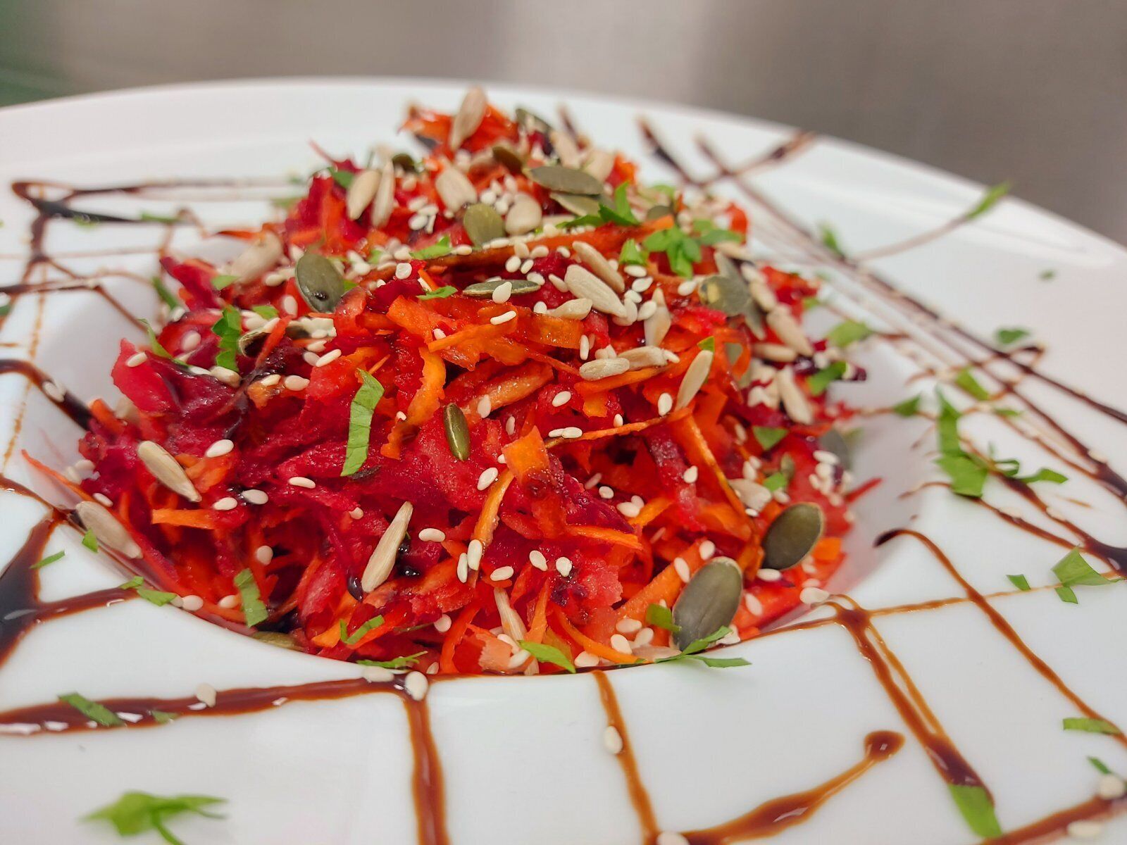 A white plate with a colorful salad topped with seeds and a drizzle of sauce.