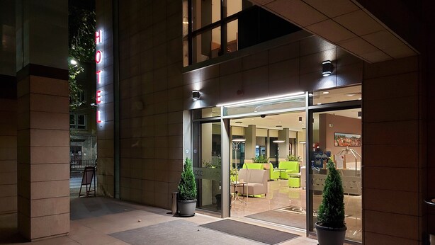 A hotel entrance with a glass door, indoor seating area visible through the door, and potted plants outside. - Hotel Puldin COOP (Plovdiv)