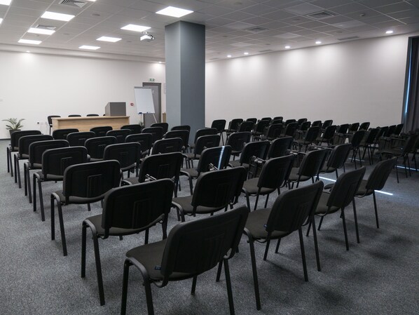 Un salón de conferencias con filas de sillas negras, un atril y una pizarra.