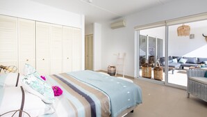 A spacious bedroom with a large bed, a balcony with seating, and a view of the outdoors.