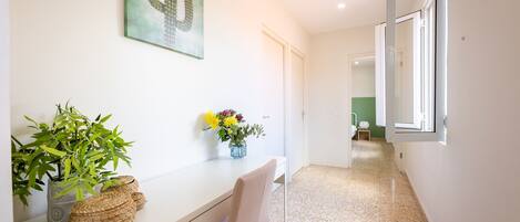 A hallway with a desk, chair, potted plants, and a cactus artwork.