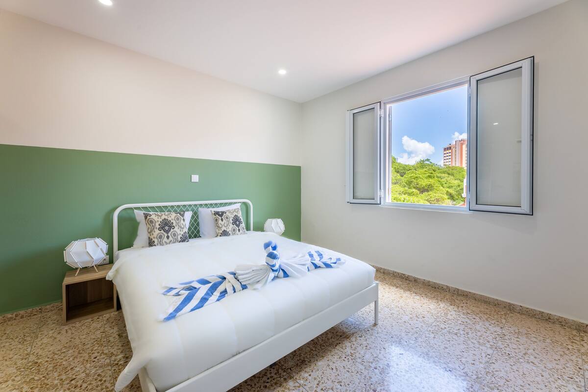Une chambre avec un lit, une table de chevet, une fenêtre donnant sur un beau paysage et un mur vert.