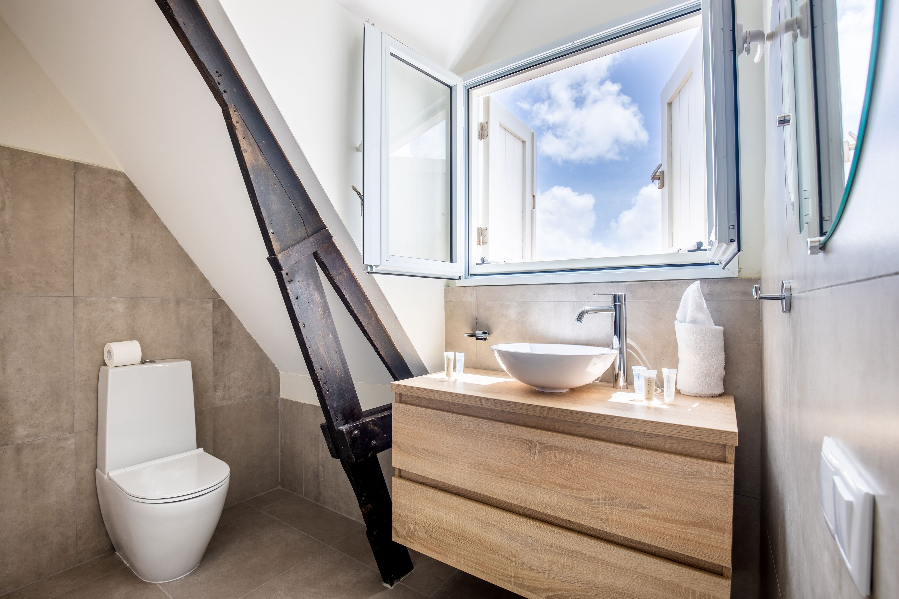 Un baño moderno con tragaluz, inodoro blanco y tocador de madera con un lavamanos grande.