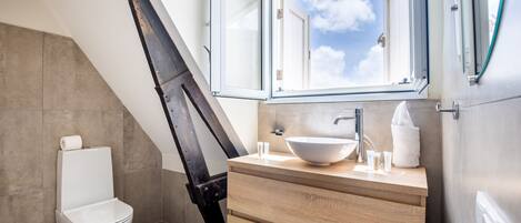 Un baño moderno con tragaluz, inodoro blanco y tocador de madera con un lavamanos grande.