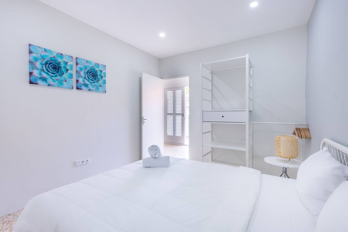 Une chambre moderne avec un lit blanc, une armoire blanche et deux œuvres d’art murales aux motifs floraux bleus.