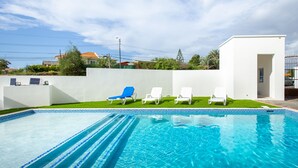 Ein Swimmingpool mit blauen Fliesen, weißen Liegestühlen und einer weißen Wand.