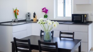 Eine moderne Küche mit weißen Schränken, einer schwarzen Arbeitsplatte, einem Esstisch mit Stühlen, einer Vase mit Blumen und einer Mikrowelle.