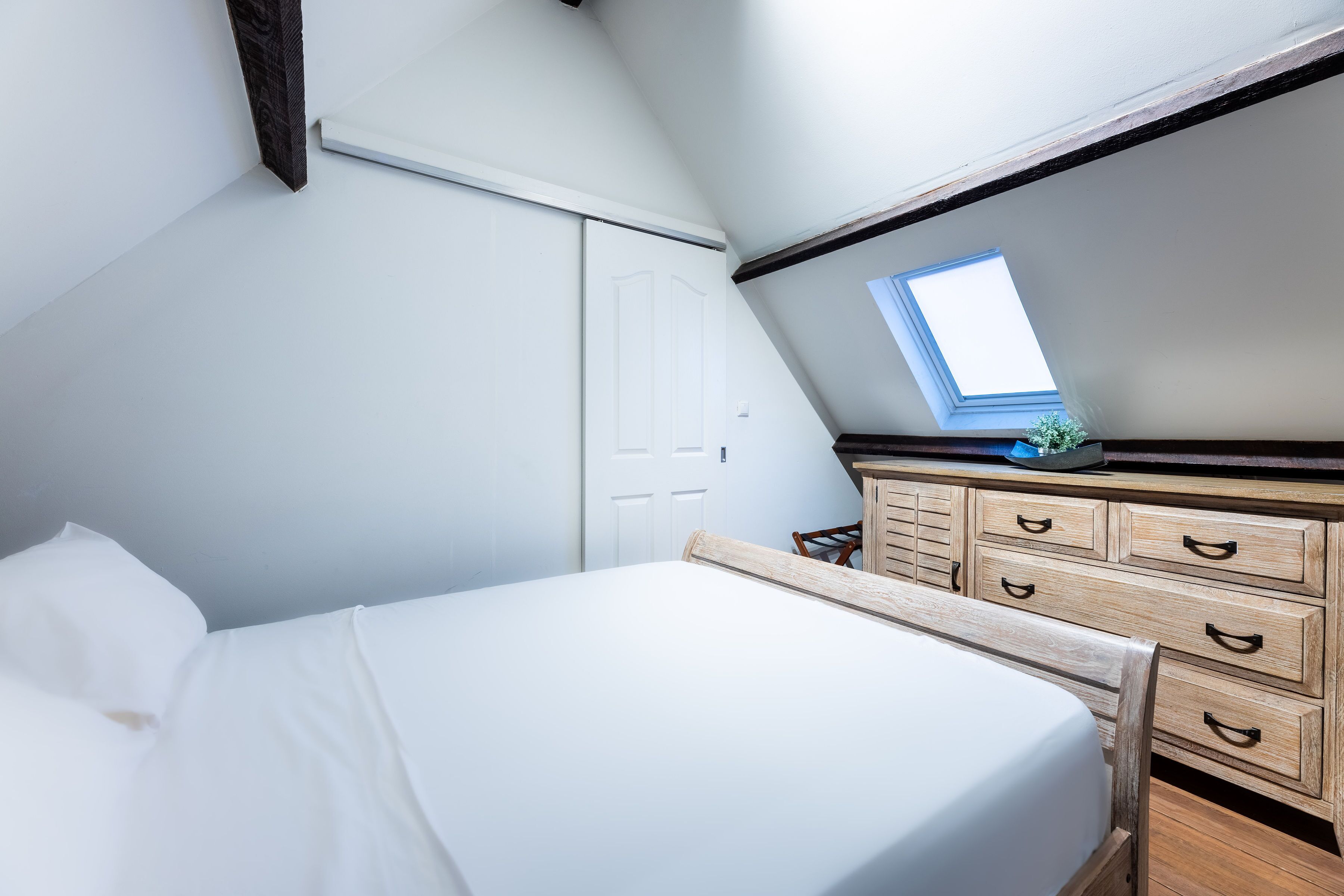 Un dormitorio con cama, cómoda, tragaluz y puerta.