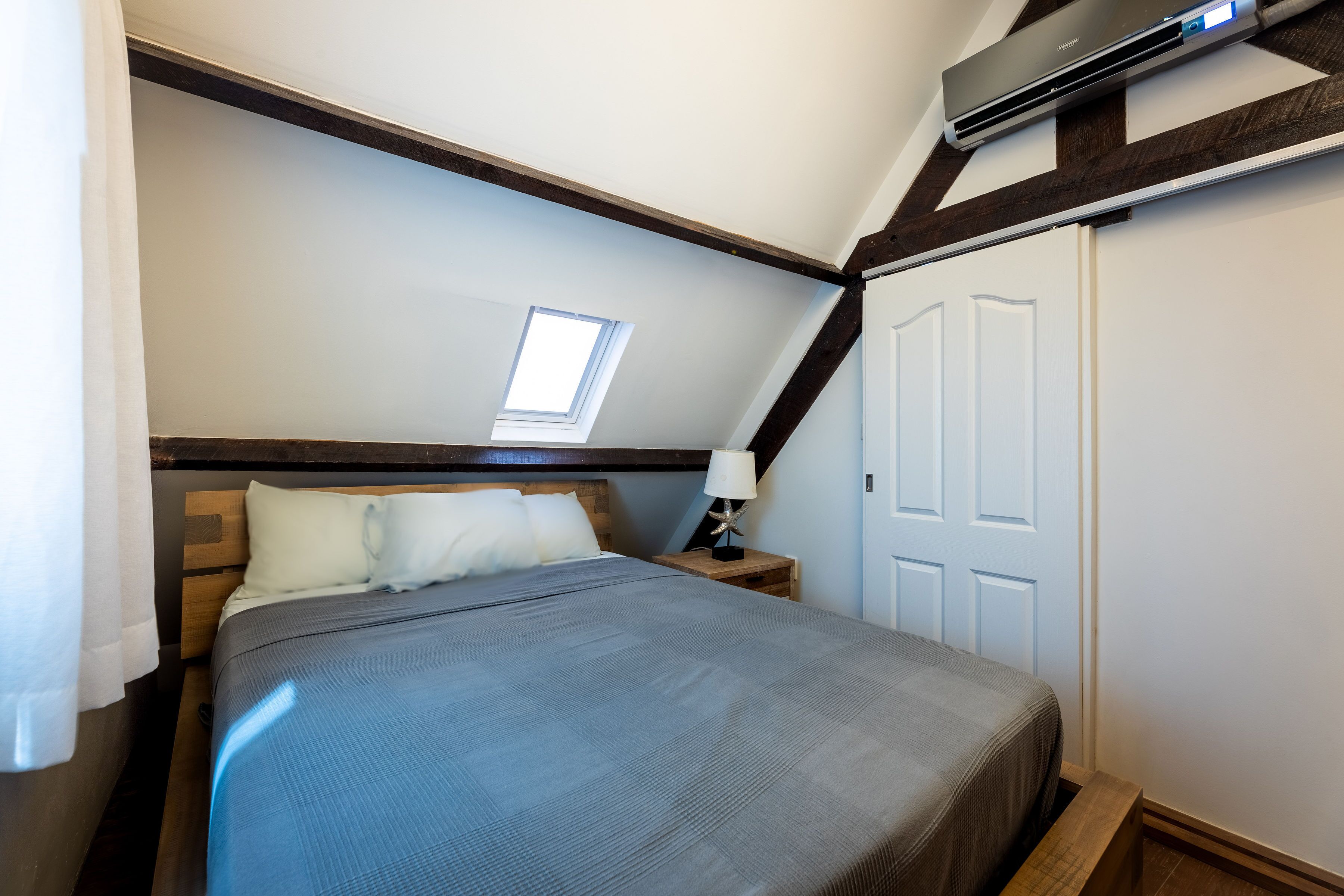 Ein Schlafzimmer mit Bett, Nachttisch, Lampe, Fenster und Klimaanlage.