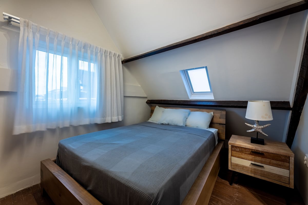 A bedroom with a bed, a nightstand, a window with a view, and a skylight.