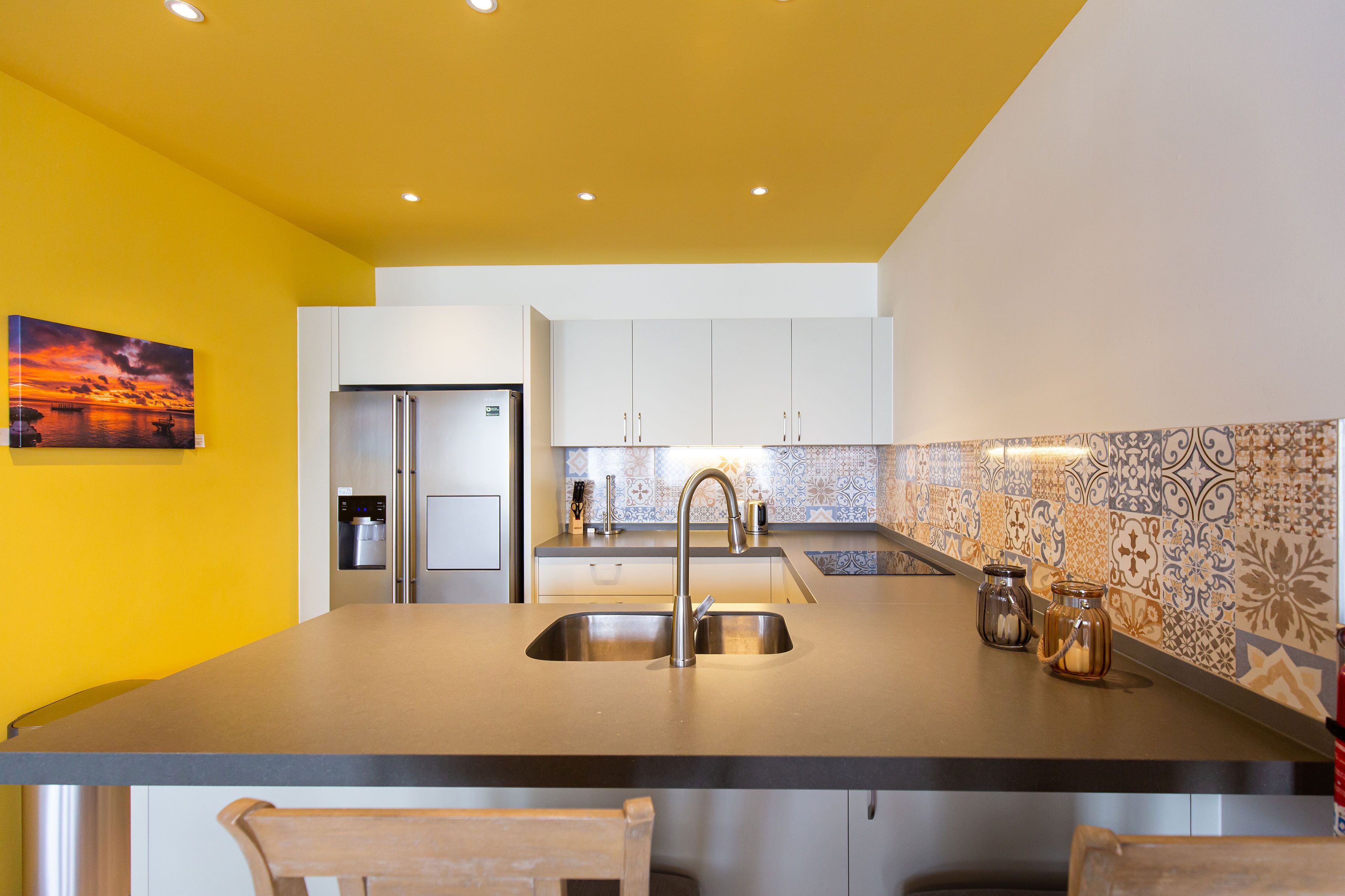 A modern kitchen with a central island, stainless steel appliances, and a yellow accent wall.