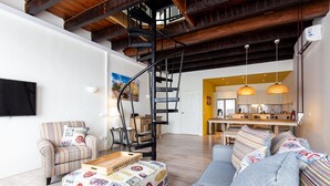 Una sala de estar moderna con una escalera, un sofá, una mesa de centro y una zona de cocina al fondo.