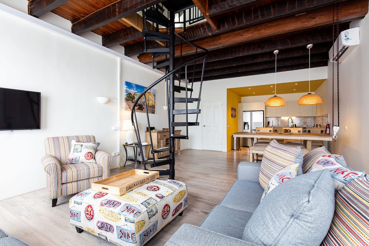 A modern living room with a staircase, a sofa, a coffee table, and a kitchen area in the background.