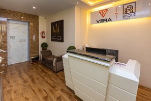 A reception area with a marble wall, a reception desk, a sofa, and a fire extinguisher. - Vera by Bisque Brookefield  (Bengaluru)