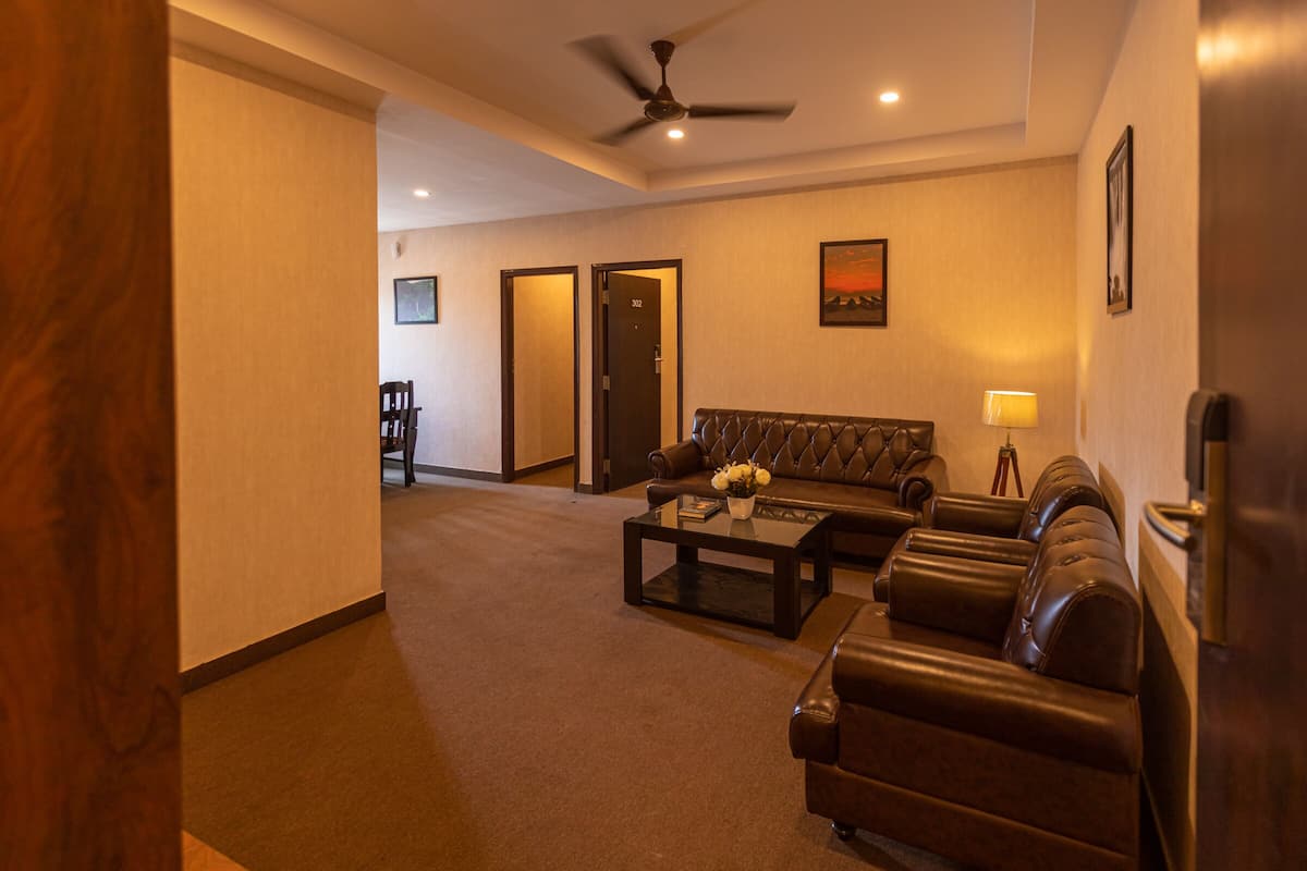 Quarto de hotel com sofá de couro, mesa de centro, ventilador de teto e quadro na parede.