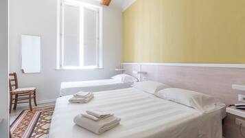 Ein Hotelzimmer mit einem großen Bett, einem kleineren Bett, einem Sessel, einem Fenster und einem Nachttisch.