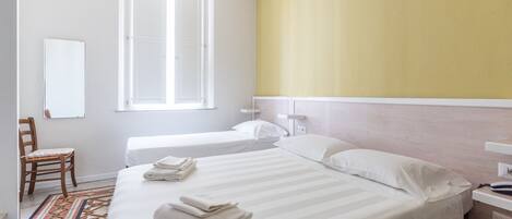 A hotel room with a large bed, a smaller bed, a chair, a window, and a bedside table.