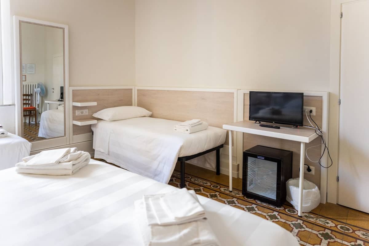A hotel room with two beds, a TV, a small fridge, and a mirror.