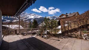Een terras met uitzicht op met sneeuw bedekte bergen, een houten pergola en een stenen muur.