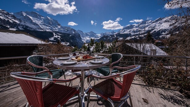 Een eettafel met stoelen en uitzicht op besneeuwde bergen.