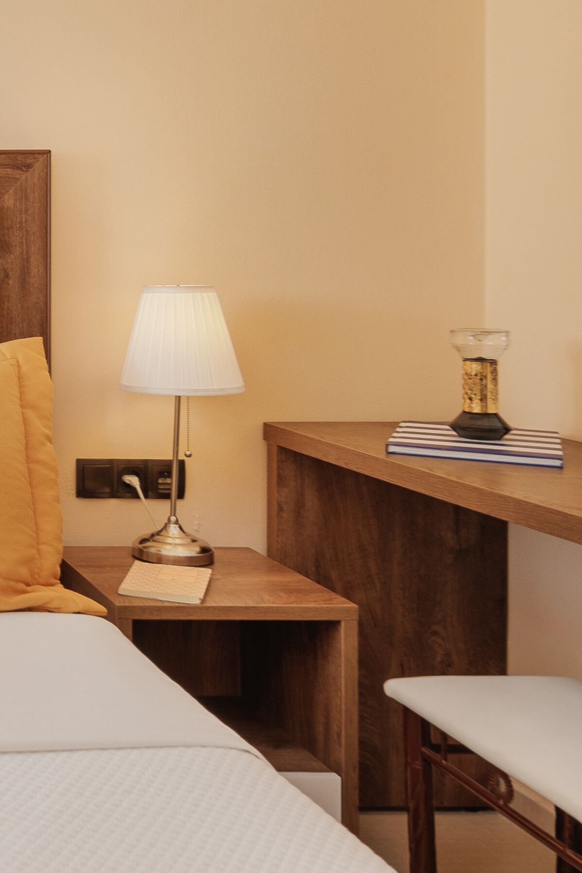 Habitación de hotel con cama, mesita de noche con lámpara, escritorio de madera pequeño y una silla.