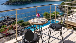 Una terraza con una mesa y dos sillas que da a una piscina y una vista panorámica de la costa.