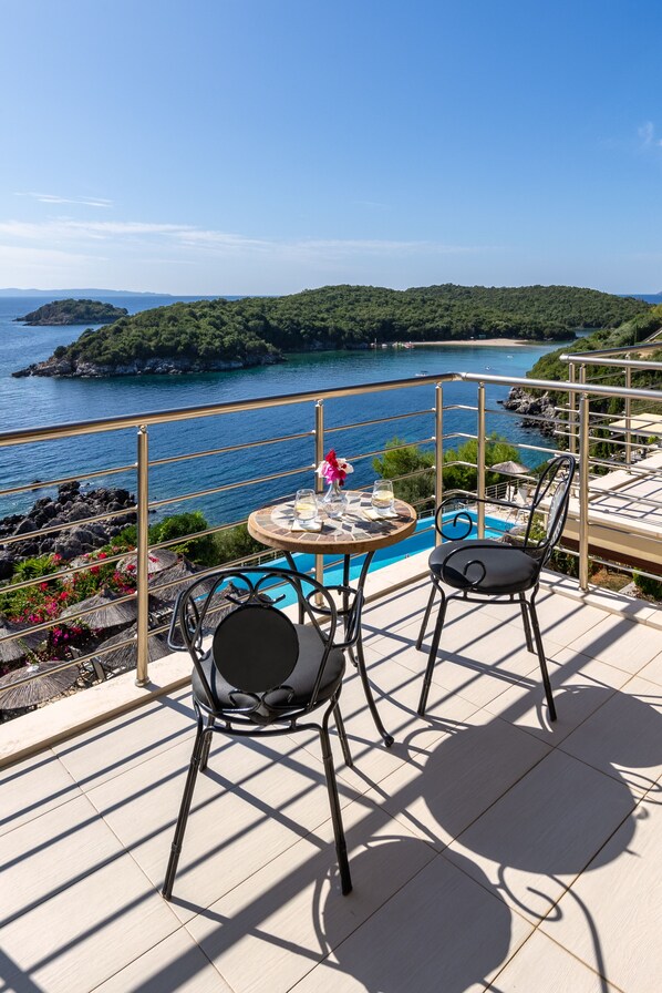 A terrace with a table and two chairs overlooking a pool and a scenic view of a coastline. - Costa Smeralda (Igoumenitsa)