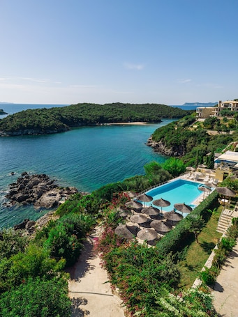 A pool area with a view of the sea, surrounded by greenery and a stone pathway.