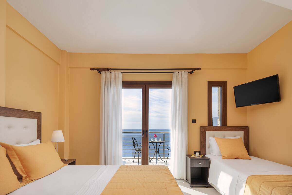 Een hotelkamer met twee bedden, een balkon met een tafel en stoelen, en een aan de muur bevestigde televisie.
