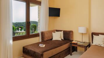 Habitación de hotel con cama, mesita de noche, lámpara, televisión y ventana con cortinas.