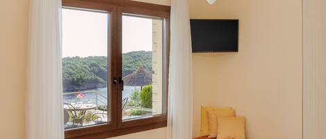 A room with a bed, a small table, a sofa, a TV mounted on the wall, and a window with curtains.