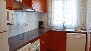 A compact kitchen with wooden cabinets, a built-in oven, a dishwasher, and a washing machine.