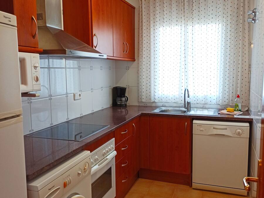A compact kitchen with wooden cabinets, a built-in oven, a dishwasher, and a washing machine.