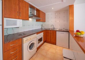 Una cocina compacta con armarios de madera, microondas integrado, lavadora y lavavajillas.