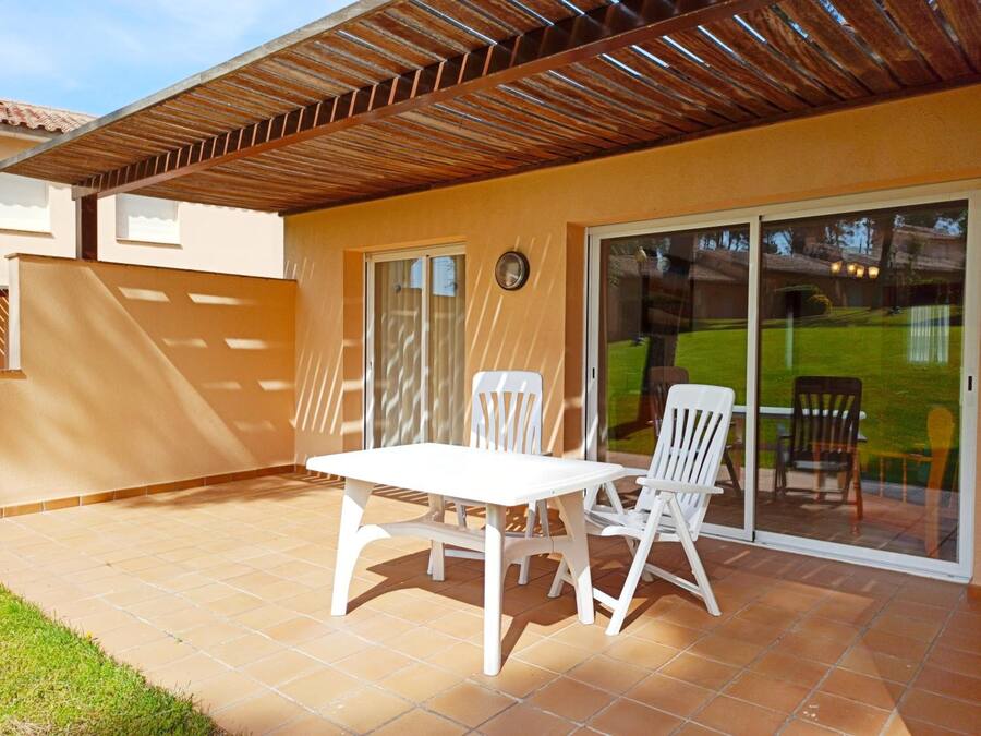 Un espacio de patio techado con una mesa y sillas, un ventanal corredero y vistas a un jardín.