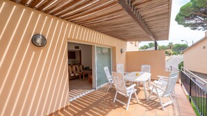 Une terrasse couverte avec une table et des chaises, une porte-fenêtre coulissante donnant sur la cuisine et une vue sur la rue.