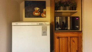 A compact kitchen with a Bosch refrigerator, a microwave, and a wooden cabinet with a potted plant. - Cyrus House Thameside (London)